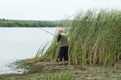 Photo of Fisherman with rod fishing near lake at summer