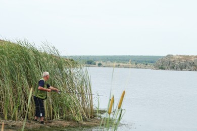 Fisherman with rod fishing near lake at summer