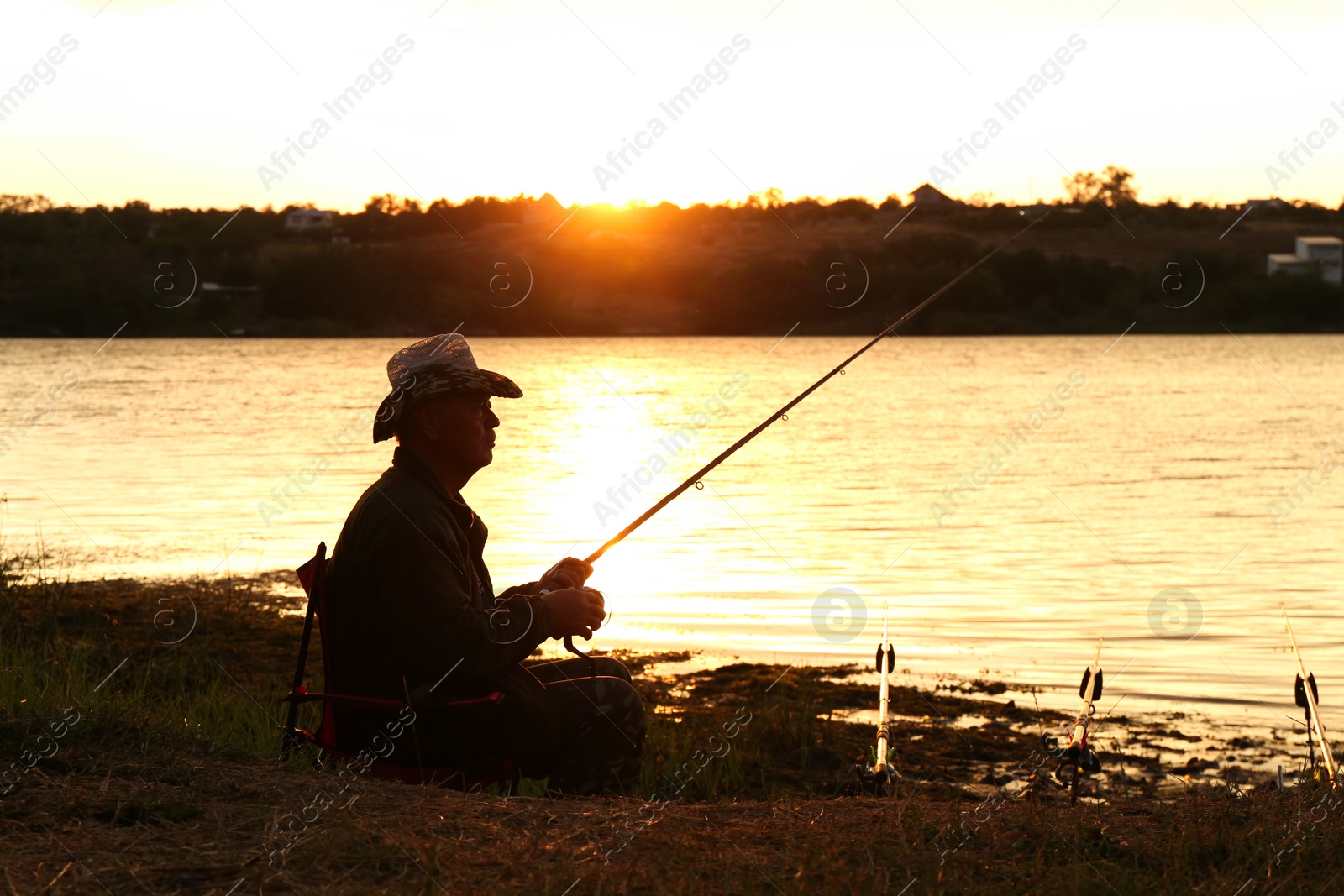 Photo of Fisherman with rod fishing near lake at sunset