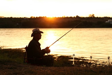 Photo of Fisherman with rod fishing near lake at sunset