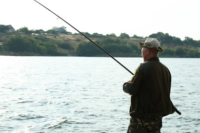 Fisherman with rod fishing near lake at summer