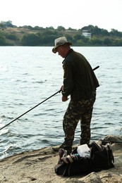 Fisherman with rod fishing near lake at summer, back view