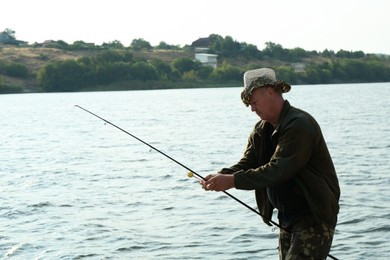 Photo of Fisherman with rod fishing near lake at summer