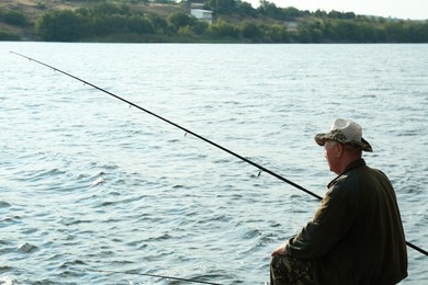 Fisherman with rod fishing near lake at summer