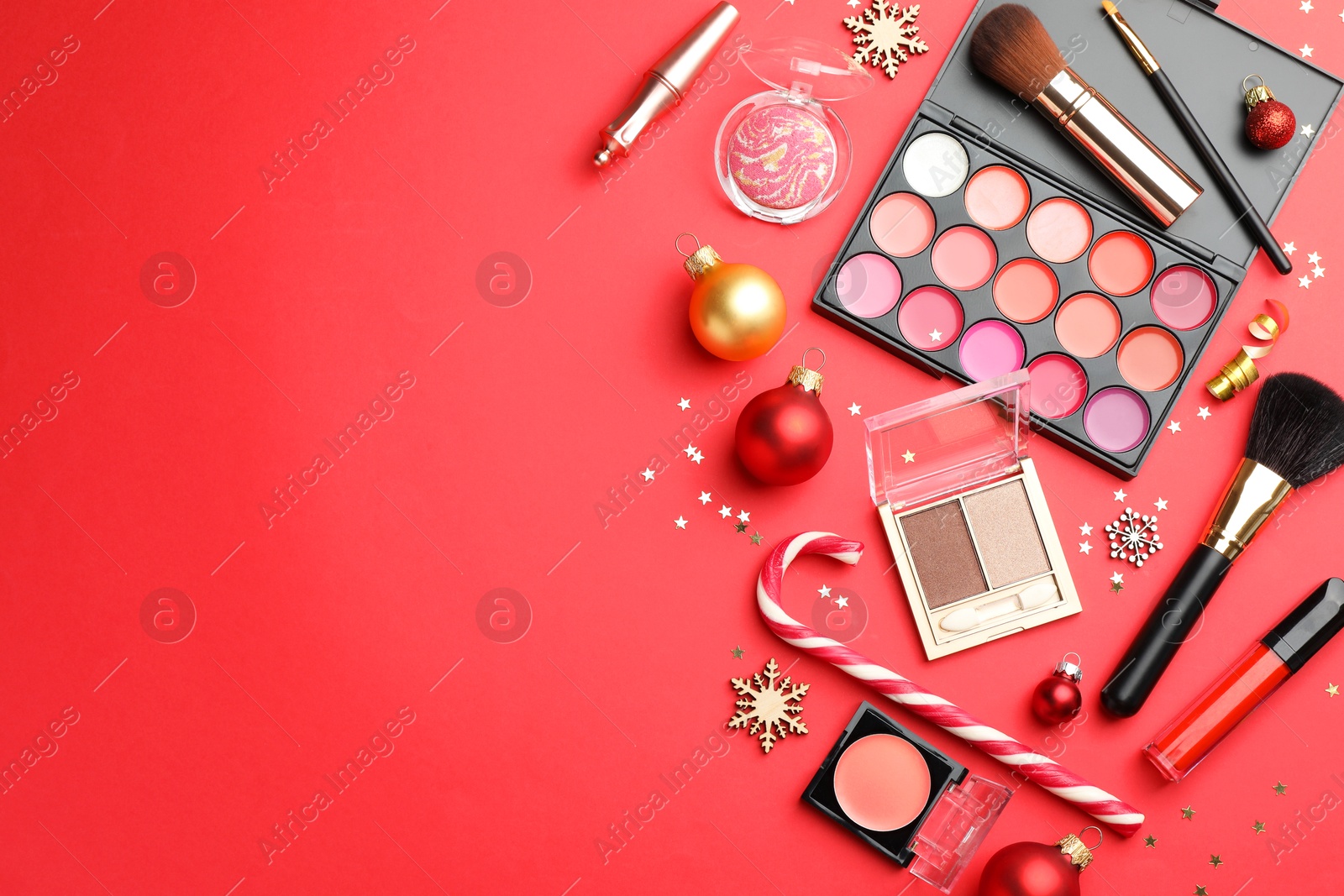 Photo of Flat lay composition with makeup products and Christmas decor on red background. Space for text