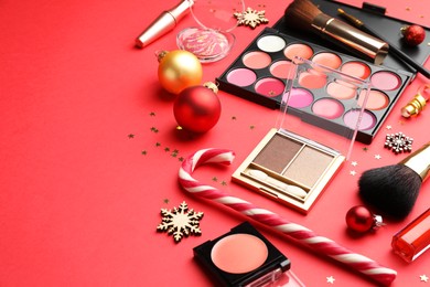 Photo of Makeup products and Christmas decor on red background, closeup