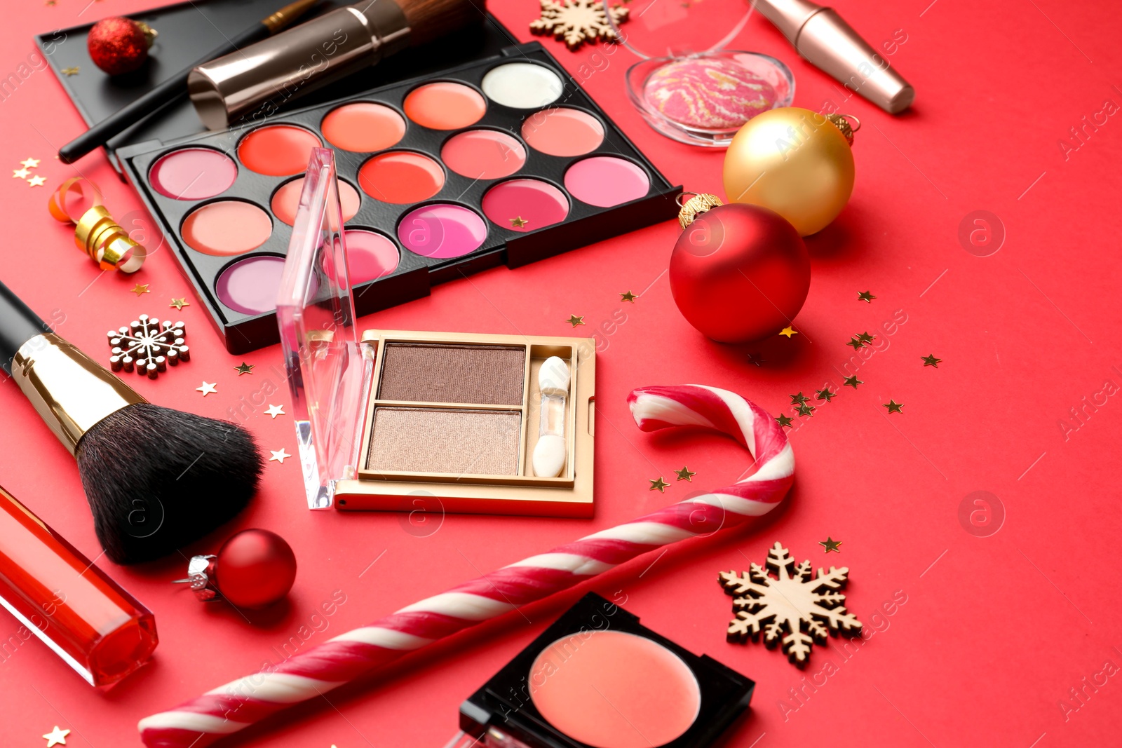 Photo of Makeup products and Christmas decor on red background, closeup