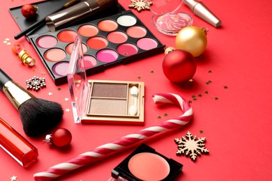 Makeup products and Christmas decor on red background, closeup