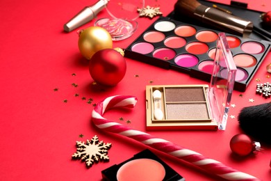 Makeup products and Christmas decor on red background, closeup