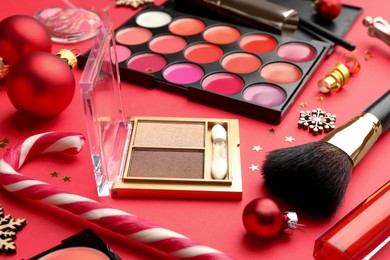 Makeup products and Christmas decor on red background, closeup