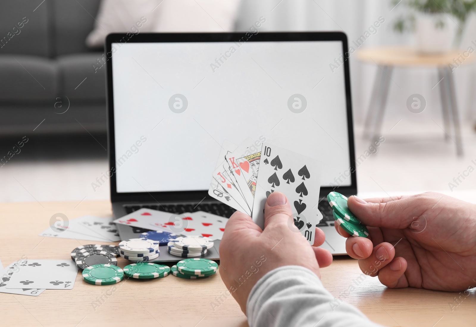 Photo of Online poker. Man with playing cards, chips and laptop at wooden table indoors, closeup