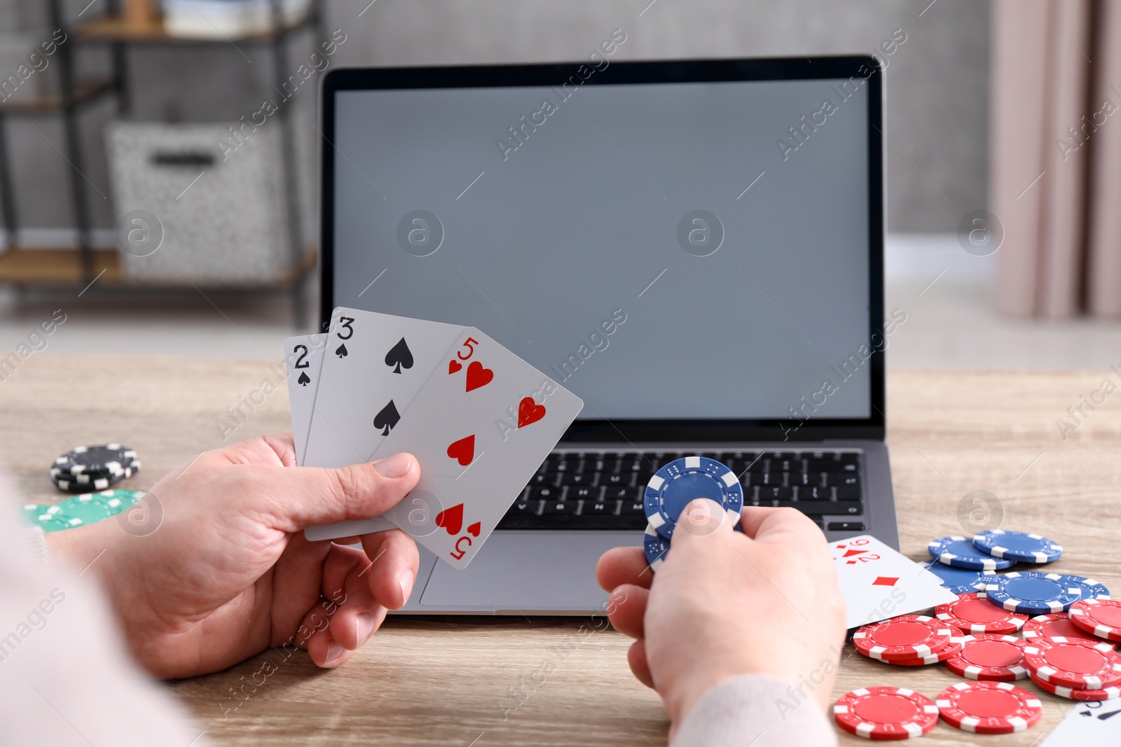 Photo of Online poker. Man with playing cards, chips and laptop at wooden table indoors, closeup