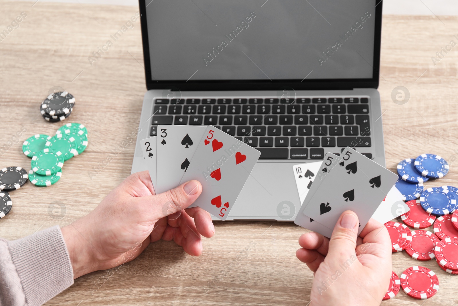 Photo of Online poker. Man with playing cards, chips and laptop at wooden table, closeup