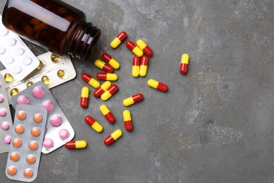 Pharmacist. Many different pills and overturned bottle on grey table, flat lay. Space for text