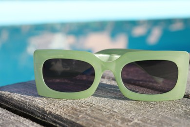 Stylish sunglasses on wooden surface, closeup. Beach accessory