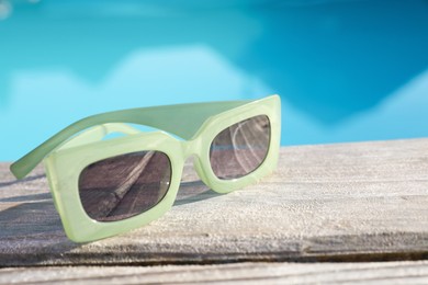 Photo of Stylish sunglasses on wooden surface, closeup. Beach accessory