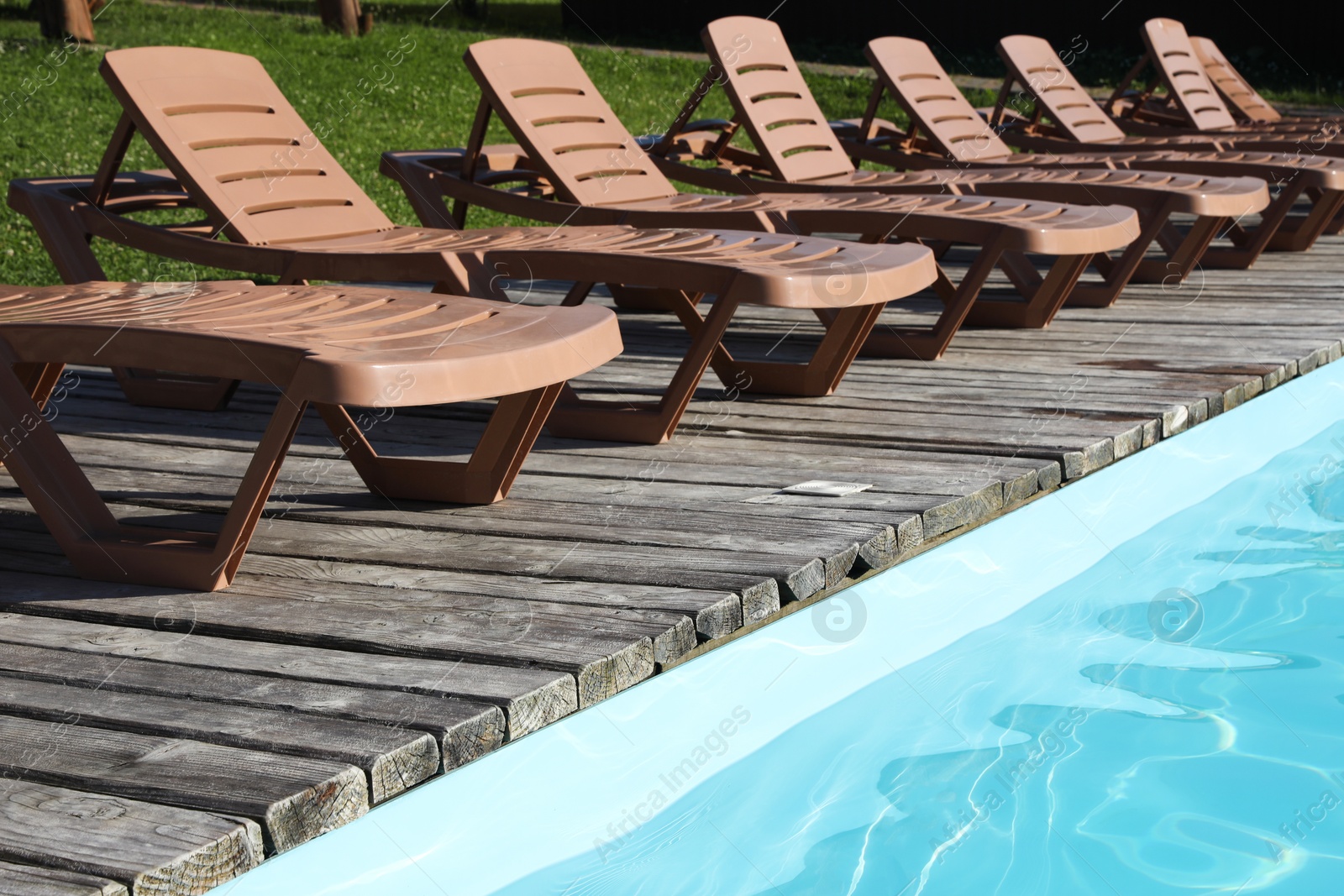 Photo of Empty sun loungers on wooden deck near outdoor swimming pool