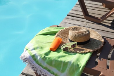 Stylish sunglasses, towel, hat and sunscreen near outdoor swimming pool. Space for text