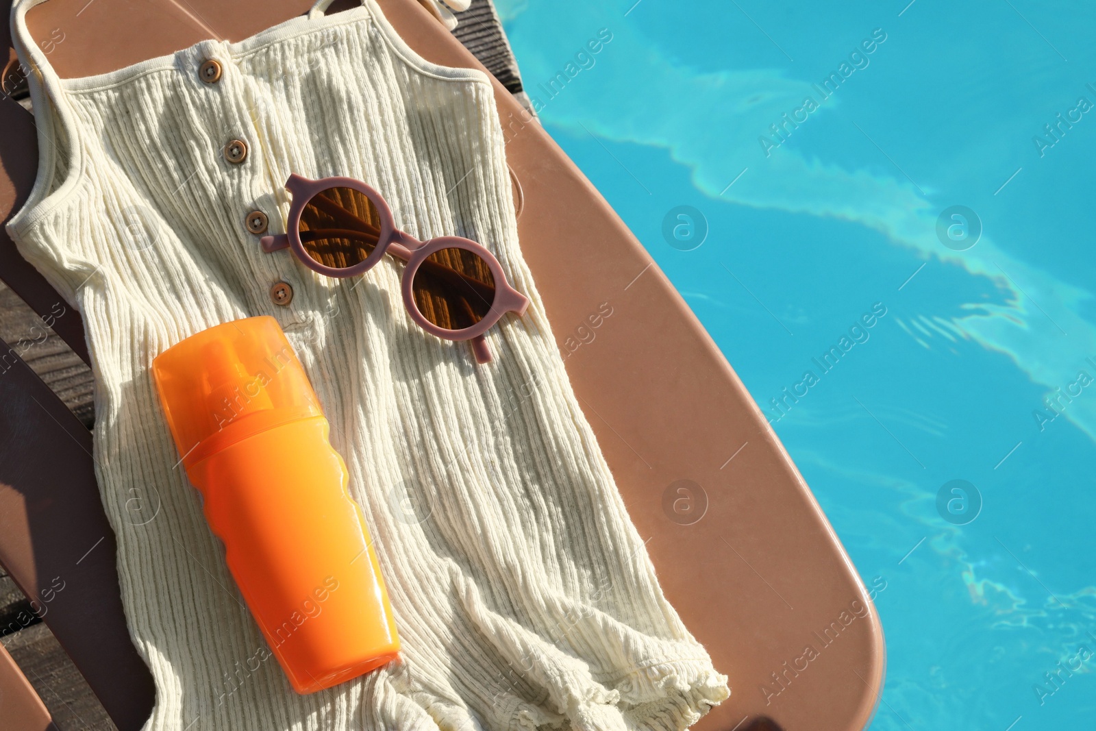 Photo of Stylish sunglasses, tank top and sunscreen on sun lounger near outdoor swimming pool, top view