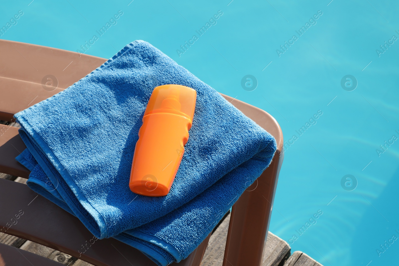 Photo of Towel and sunscreen on sun lounger near outdoor swimming pool