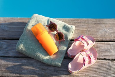 Stylish sunglasses, shoes, towel and sunscreen on wooden deck near outdoor swimming pool, top view