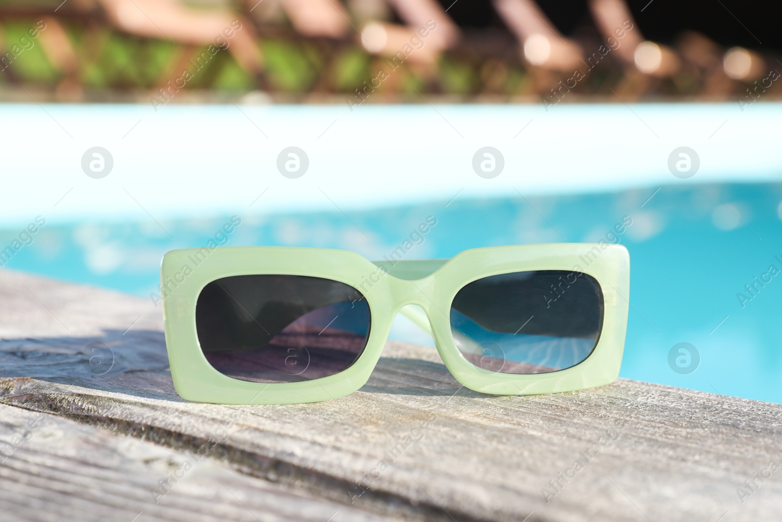 Photo of Stylish sunglasses on wooden deck near outdoor swimming pool