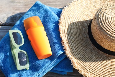 Photo of Stylish sunglasses, hat, towel and sunscreen on wooden deck, top view