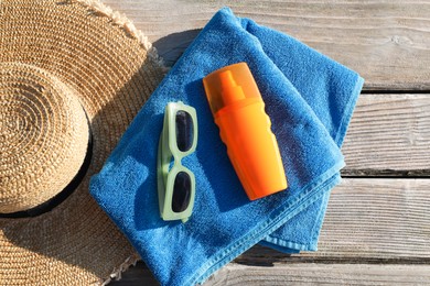 Photo of Stylish sunglasses, hat, towel and sunscreen on wooden deck, top view