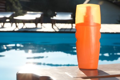 Photo of Sunscreen on sun lounger near outdoor swimming pool on sunny day. Space for text