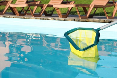 Cleaning swimming pool with skimmer net on sunny day