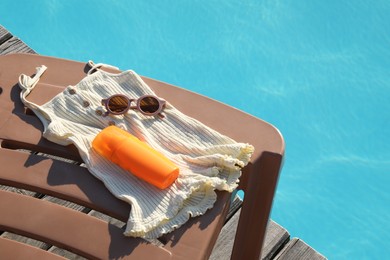 Photo of Stylish sunglasses, tank top and sunscreen on sun lounger near outdoor swimming pool