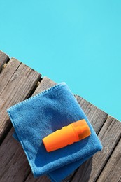 Photo of Towel and sunscreen on wooden deck near outdoor swimming pool, top view