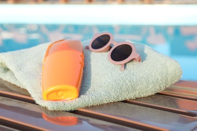 Photo of Stylish sunglasses, towel and sunscreen on wooden deck near outdoor swimming pool