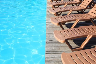 Photo of Empty sun loungers on wooden deck near outdoor swimming pool