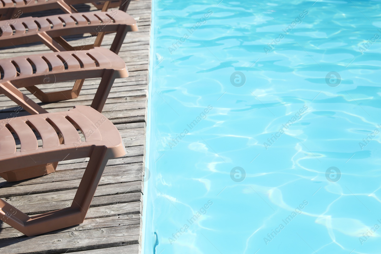 Photo of Empty sun loungers on wooden deck near outdoor swimming pool