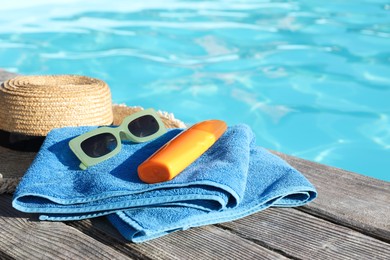 Photo of Stylish sunglasses, towel, hat and sunscreen on wooden deck near outdoor swimming pool