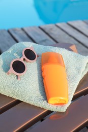 Stylish sunglasses, towel and sunscreen on sun lounger near outdoor swimming pool