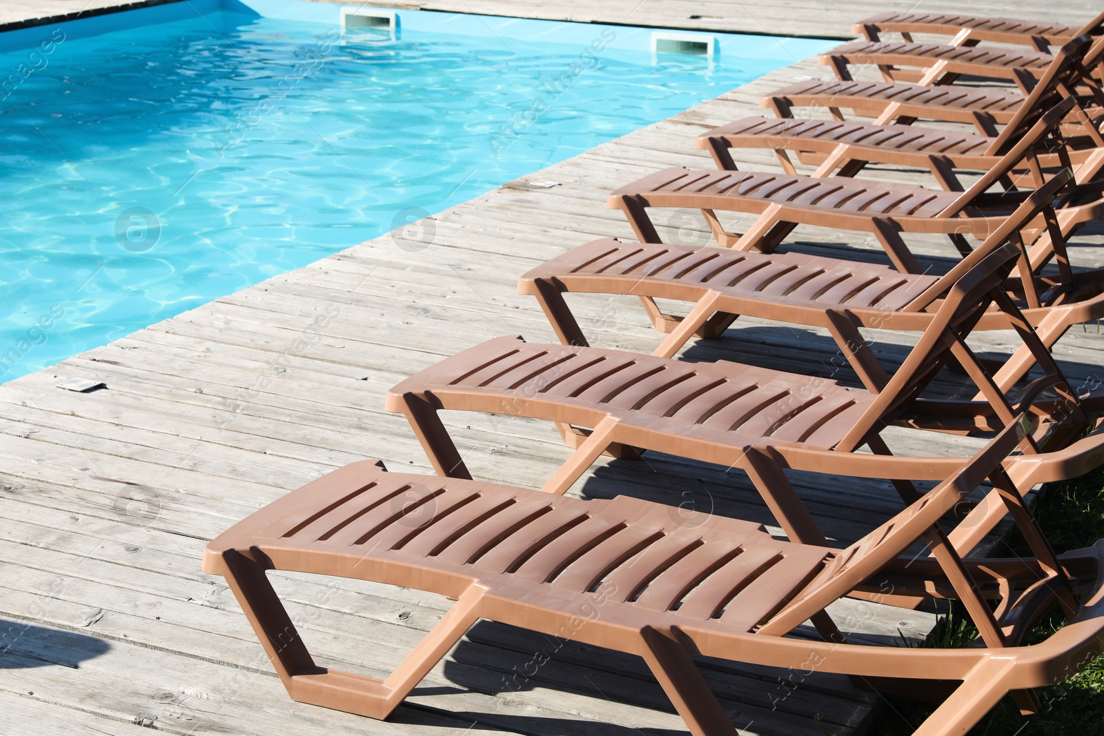 Photo of Empty sun loungers on wooden deck near outdoor swimming pool