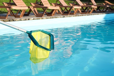 Cleaning swimming pool with skimmer net on sunny day