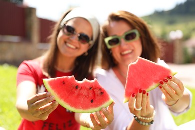 Happy women holding slices of juicy watermelon outdoors, selective focus