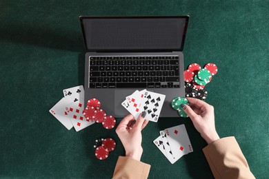 Photo of Online poker. Woman holding playing cards and chips at green table with laptop, top view