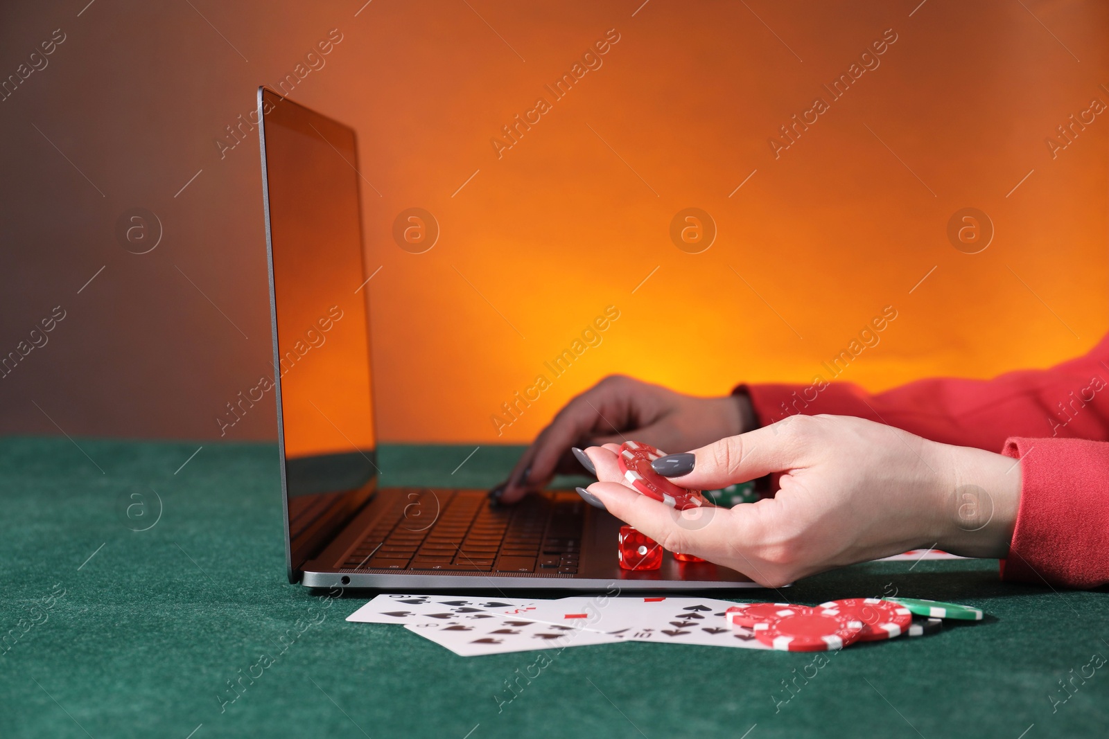 Photo of Online poker. Woman holding chips and using laptop at green table, closeup