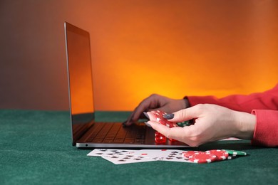 Photo of Online poker. Woman holding chips and using laptop at green table, closeup