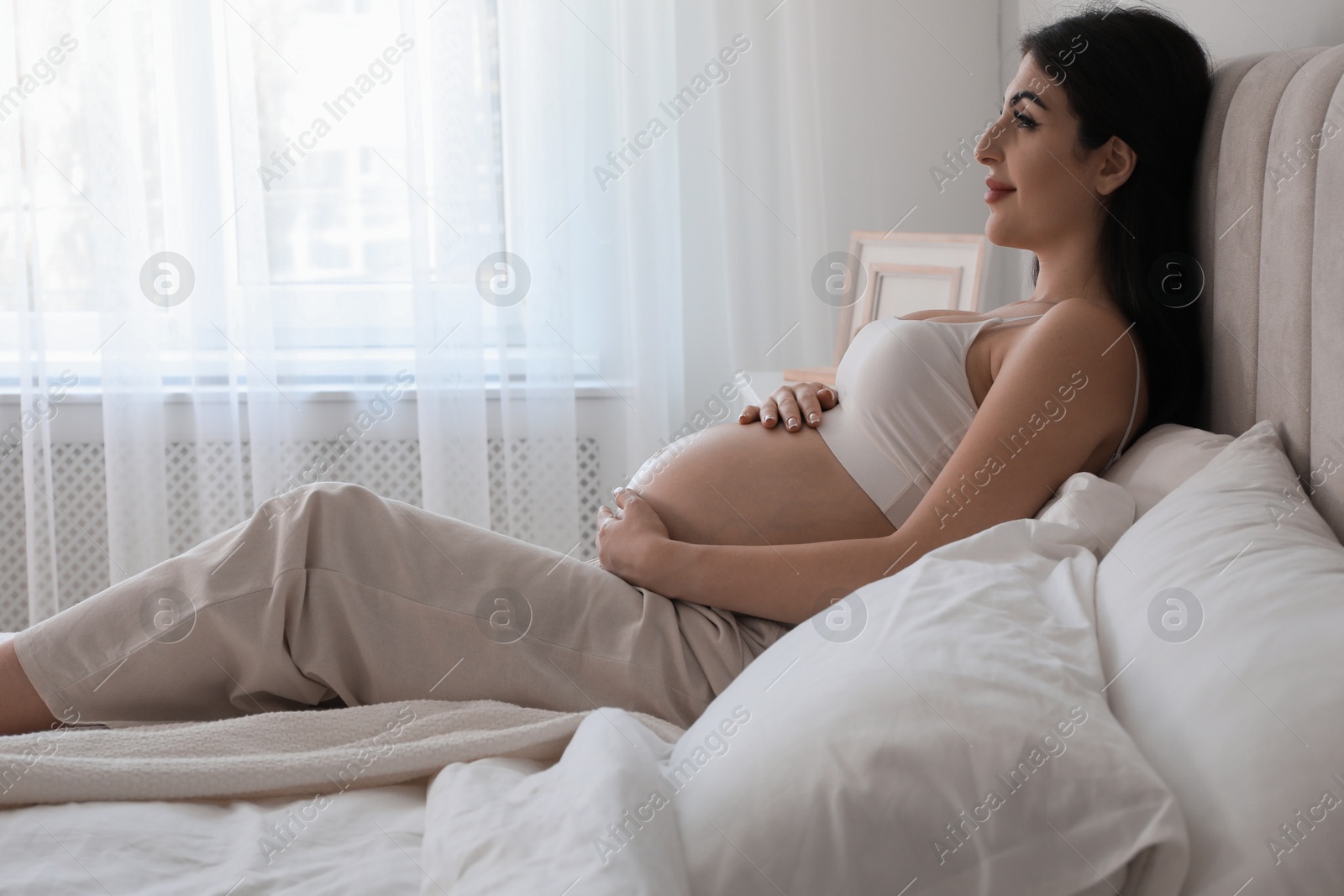 Photo of Young pregnant woman lying on bed at home