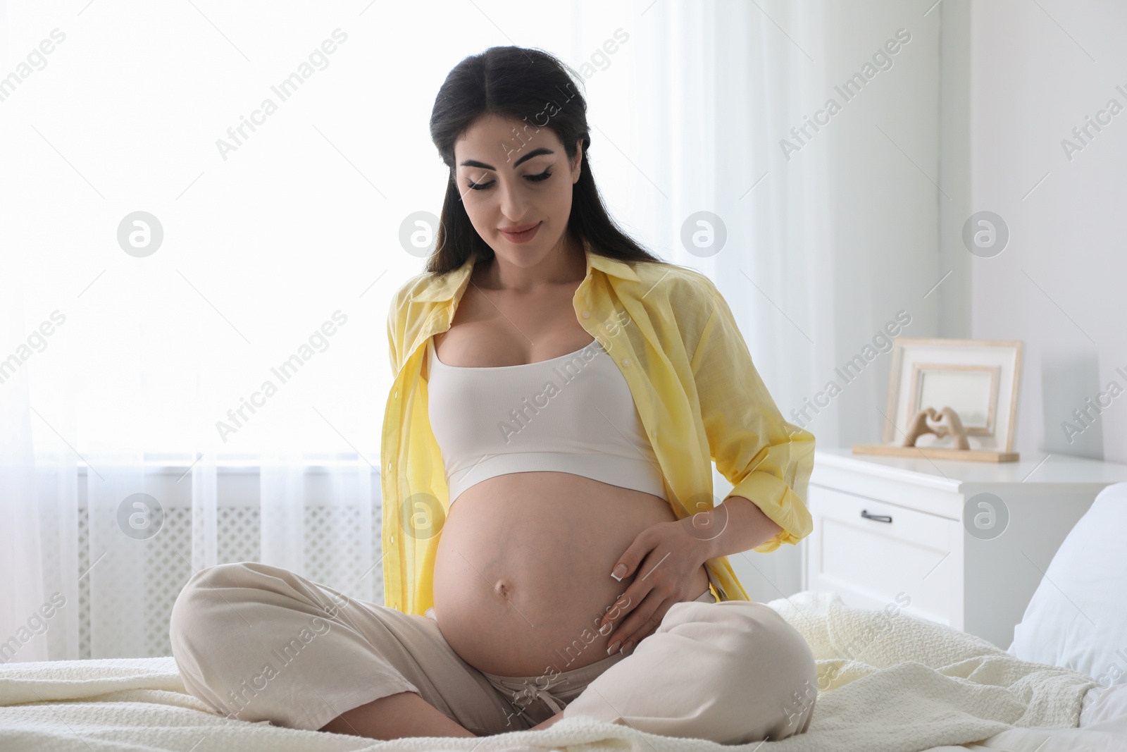 Photo of Young pregnant woman sitting on bed at home