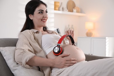 Photo of Young pregnant woman with headphones on belly at home