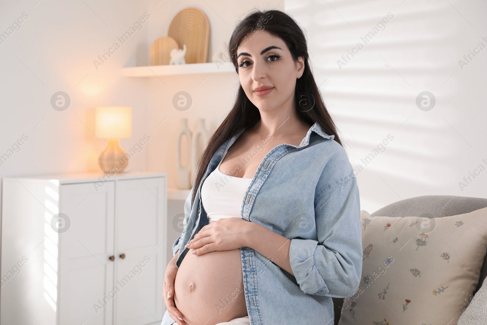 Photo of Young pregnant woman sitting on sofa at home