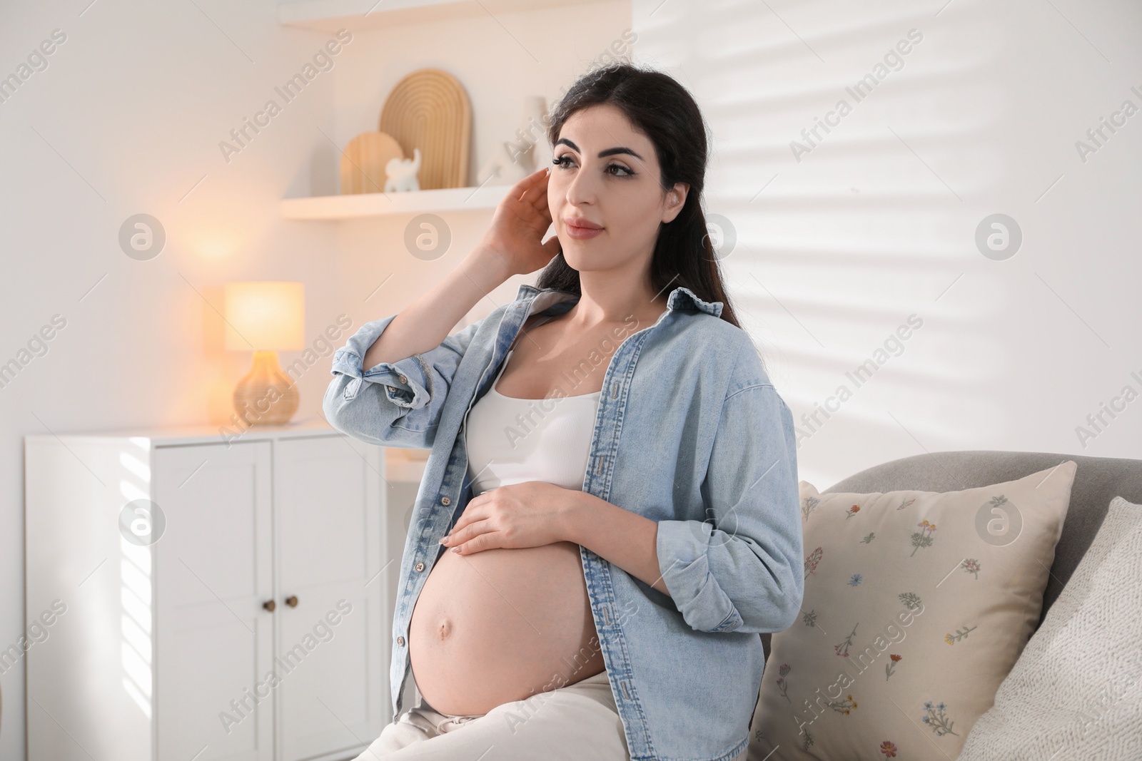 Photo of Young pregnant woman sitting on sofa at home