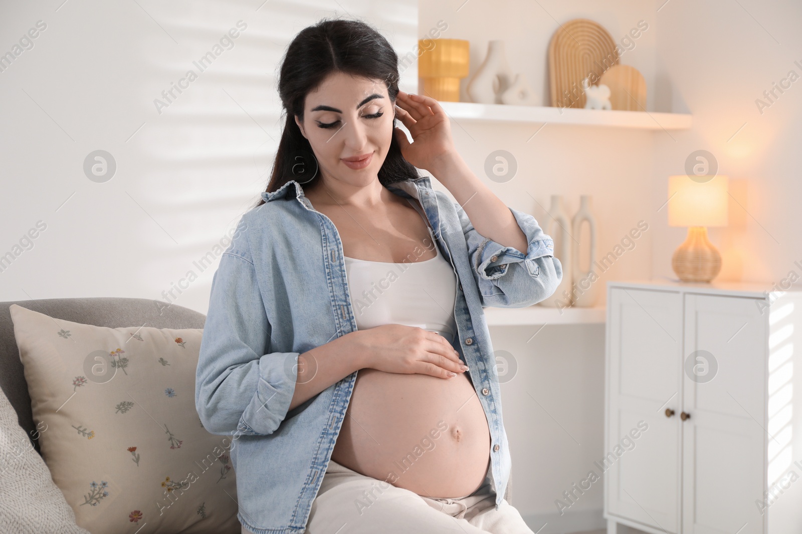 Photo of Young pregnant woman sitting on sofa at home