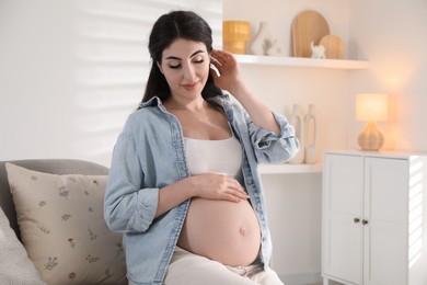 Photo of Young pregnant woman sitting on sofa at home